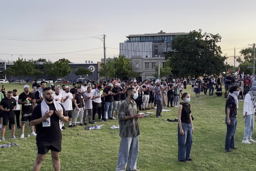 People stand in a park for a prayer service at sunset.