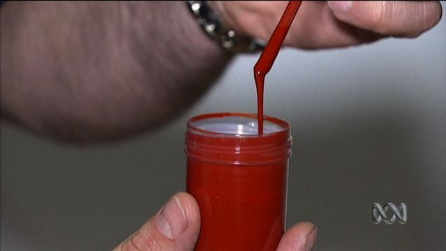 Hands hold a small jar with bright red liquid dribbling from a small stick