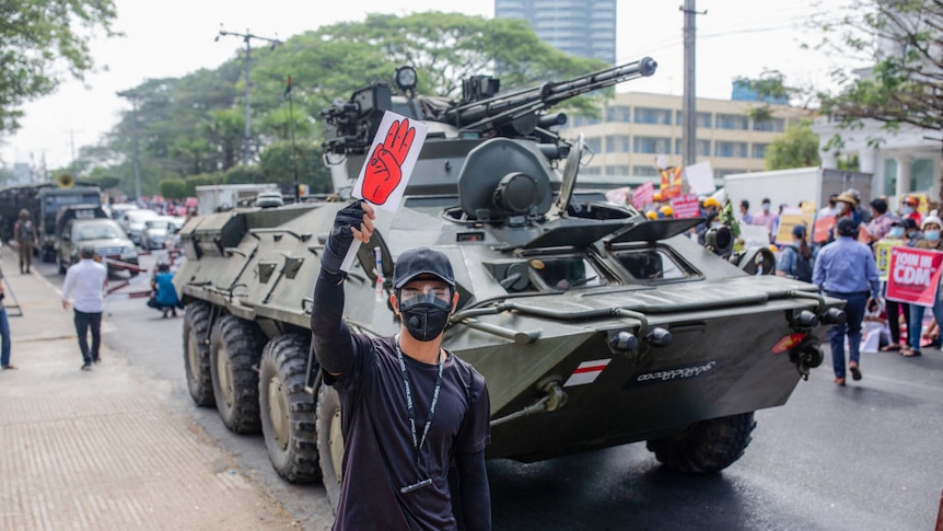 A protester holds a placard with a three fingered salute in front of a military tank in front  of the Central Bank building