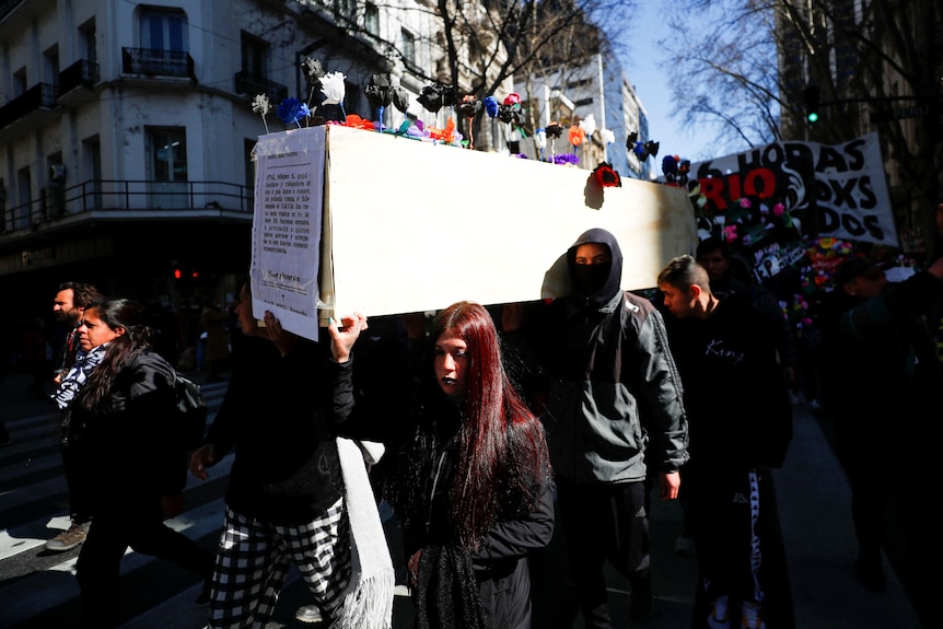 A group of people carrying a coffin with a sheet of paper on the front