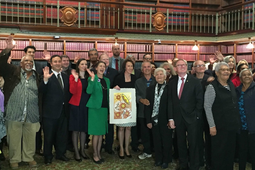 A group photo of MPs with survivors of the Stolen Generation inside Parliamentary chambers.