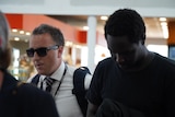 A young black man walks through the airport being ushered by a police officer in a white button up shirt