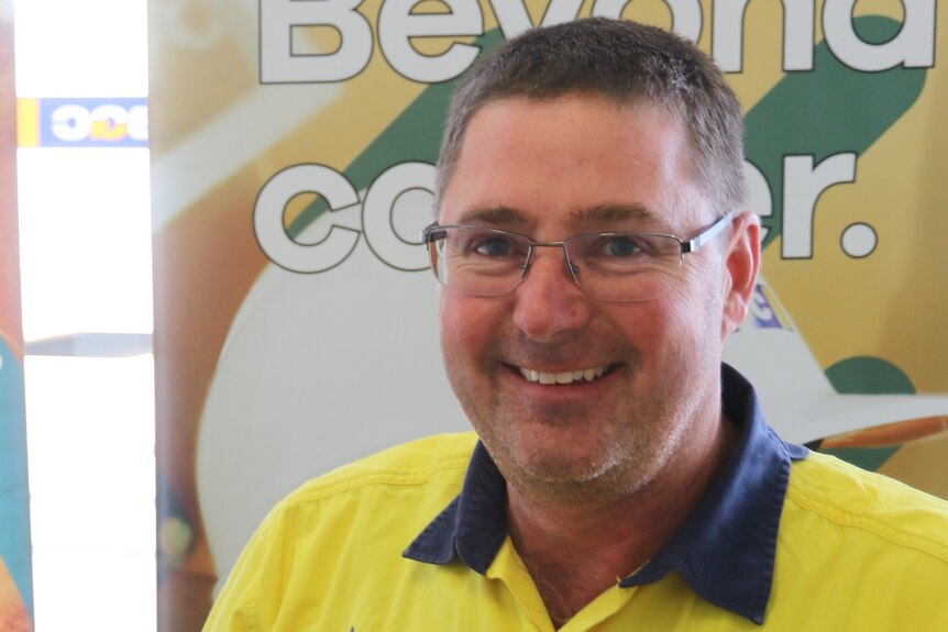 Man wearing glasses in foreground left, head and chest visible, mining signs in the background