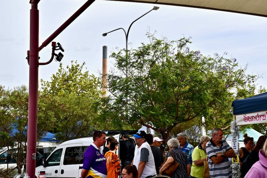 A group of people at markets with the Port Pirie lead smelter in the background.
