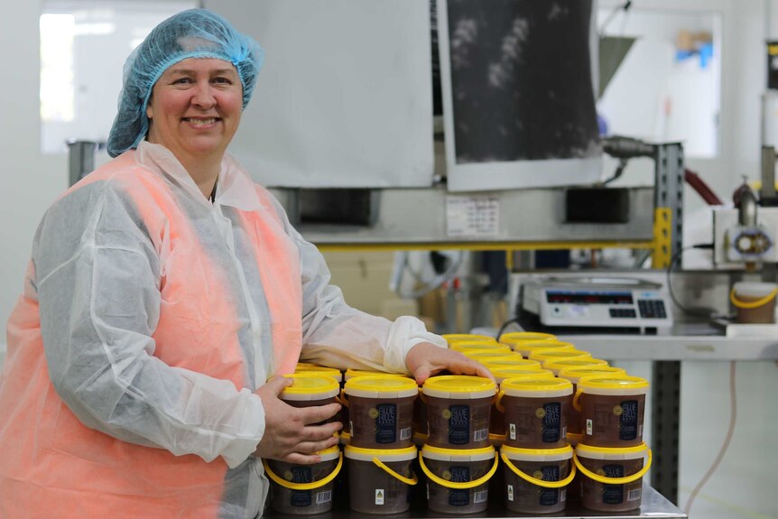A woman stands in front of a table of buckets of honey inside a factory.
