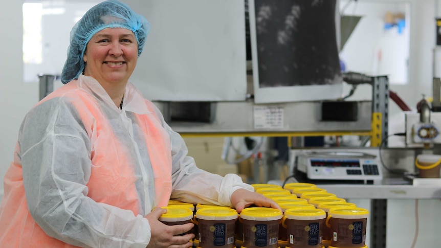 a woman stands in front of a table of buckets of honey inside a factory
