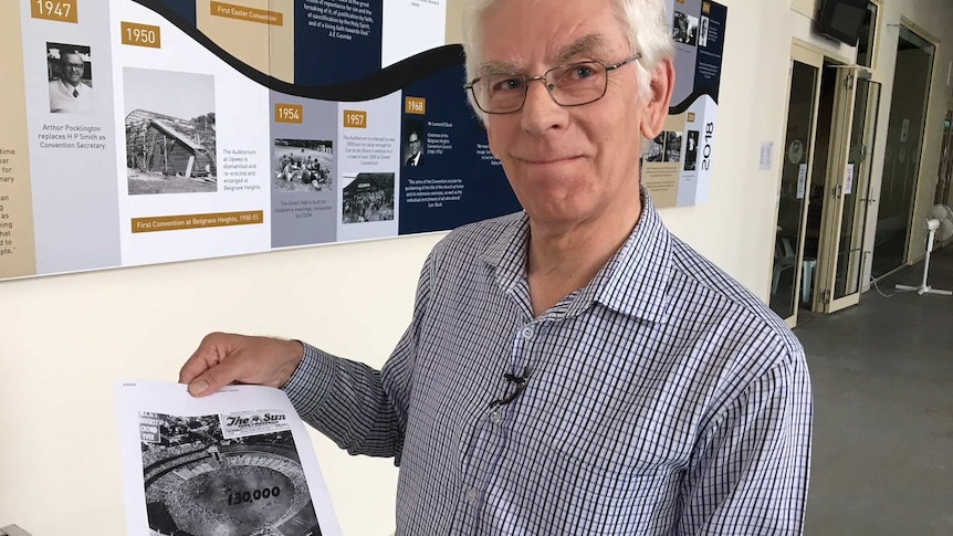 Geoff Gawler holding a newspaper article about Billy Graham's MGC visit.