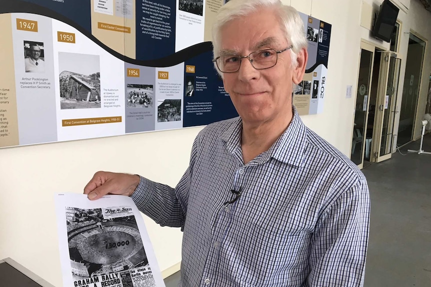 Geoff Gawler holding a newspaper article about Billy Graham's MGC visit.