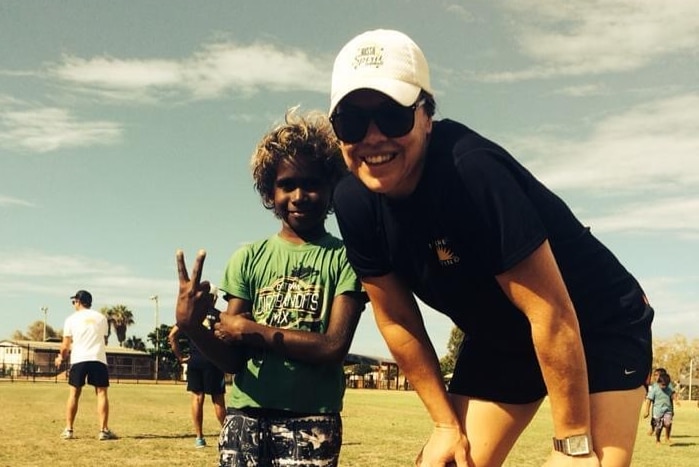 Stacey Porter stands next to an Indigenous boy who is holding his fingers up in a peace sign.