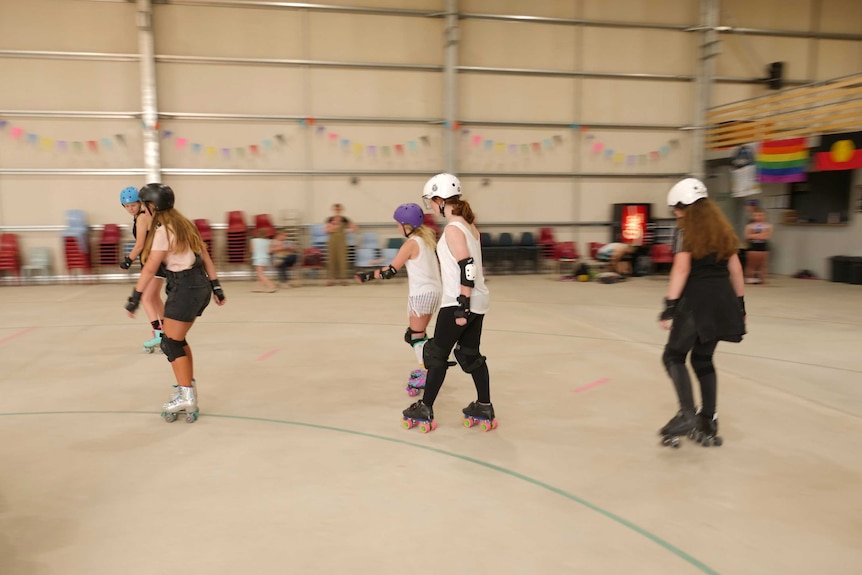 Five girls skating around a concrete rink.