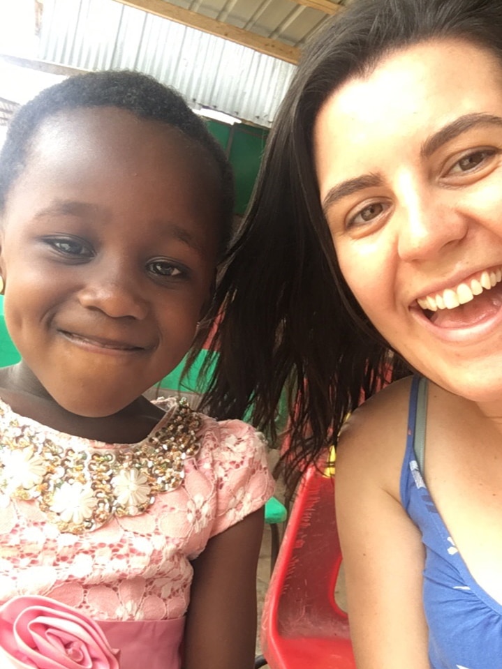 A young Caucasian woman takes a smiling selfie with a young girl of African appearance.