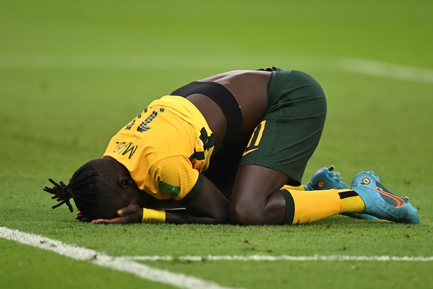 A soccer player wearing green and yellow puts his head in his hands in celebration