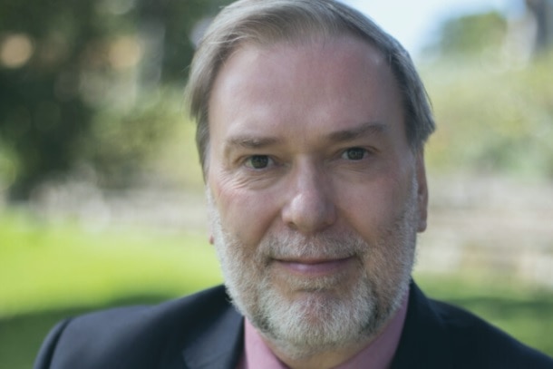 A white-bearded man, wearing a suit and tie, sitting outdoors.