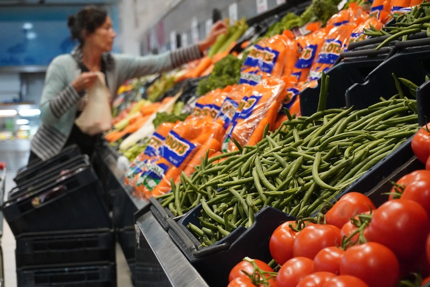A woman in a grocery aisle of fruit and vegetables.