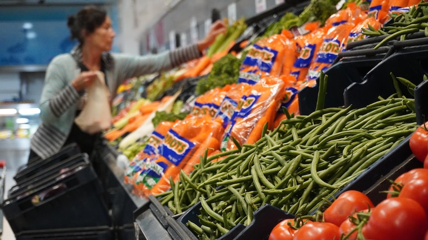 一位妇女在摆满水果和蔬菜的杂货铺购物