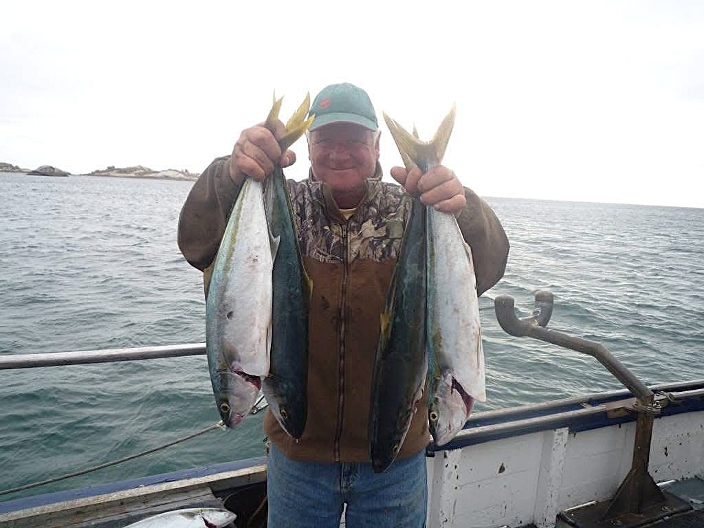 A man holds two fish while standing on a boat.