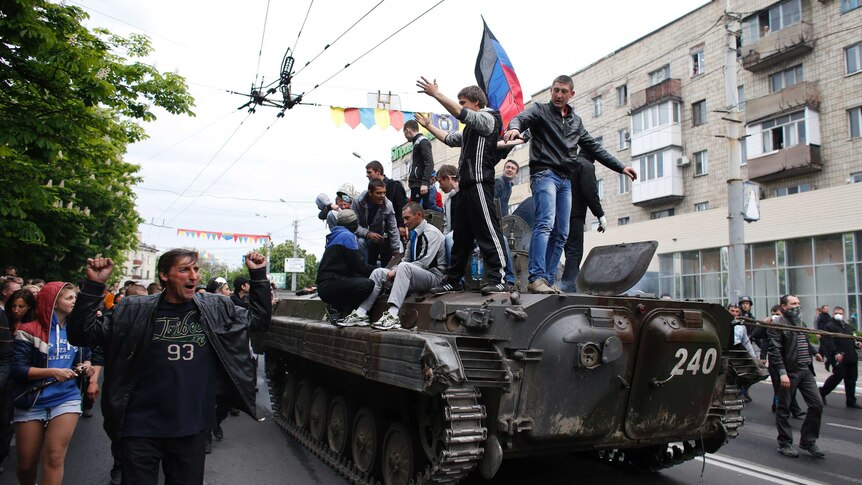 People climb a broken armoured vehicle left behind after Ukrainian forces in Mariupol.