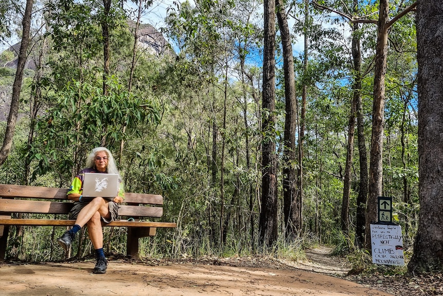 woman sits on beach bench with mountain in background