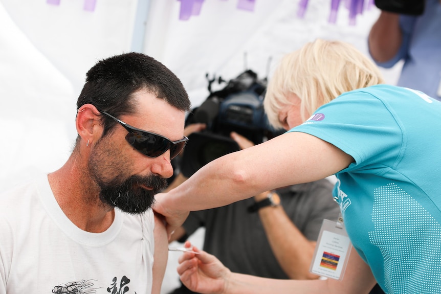 A man receiving a COVID-19 vaccine from a woman in a blue shirt.