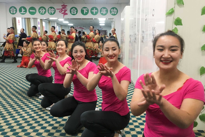 Women in matching pink shirts and large smiles pose for a camera.