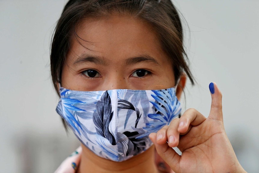 A woman with a mask shows a finger with blue ink to demonstrate she has voted.