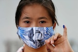 A woman with a mask shows a finger with blue ink to demonstrate she has voted.