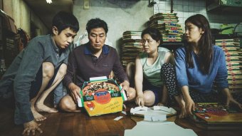 The family of four who are the main characters of Parasite crowd around a board game.