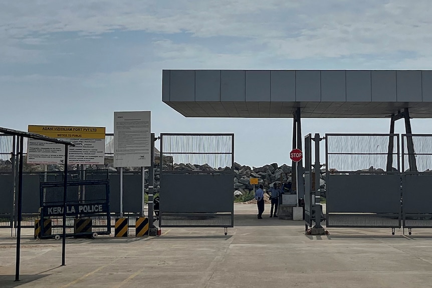 A metal gate sits open with two security guards standing just beyond them. 