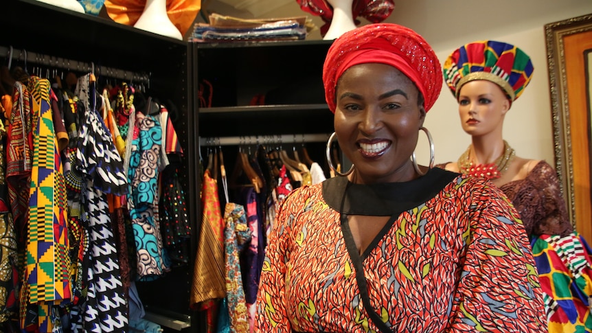 Nigerian fashion designer Safuratu Bakare with a bright red hat and big earings with a colourful clothes rack in the background