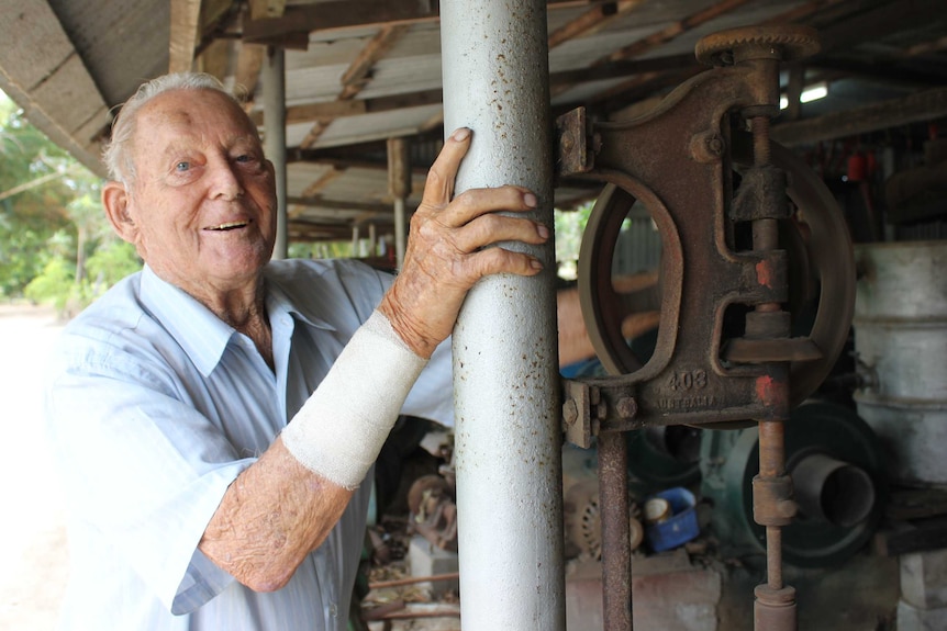 A smiling man steadies himself on a pole as he turns the wheel of an antique piece of farming machinery