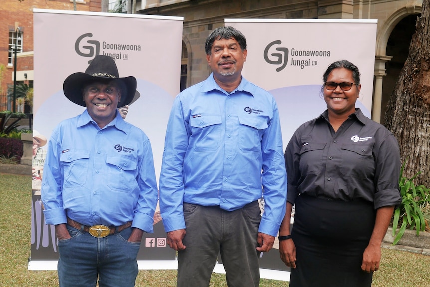 Two men wearing blue shirts and a woman wearing all black stand together for a photo