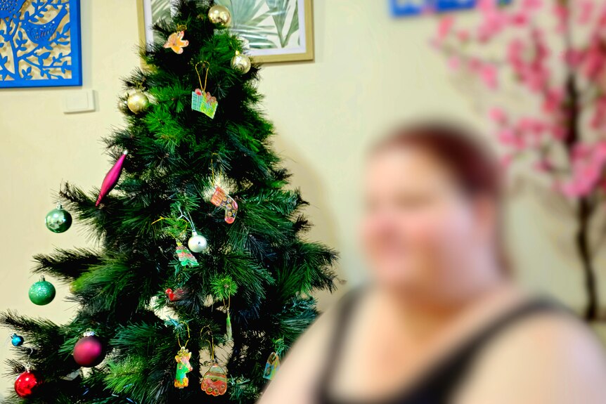 A blurred out woman sits in front of a Christmas tree