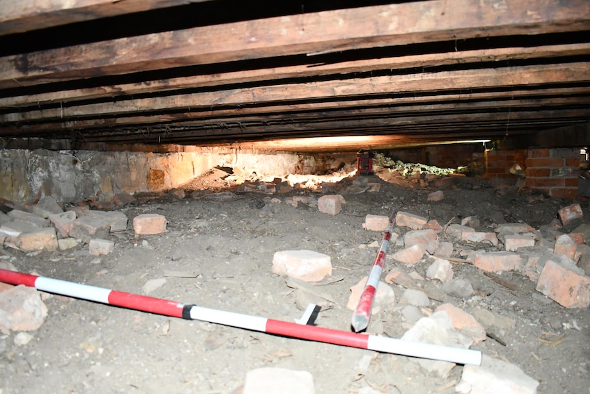 The image shows a dirty, cramped space littered with old bricks under a low ceiling.