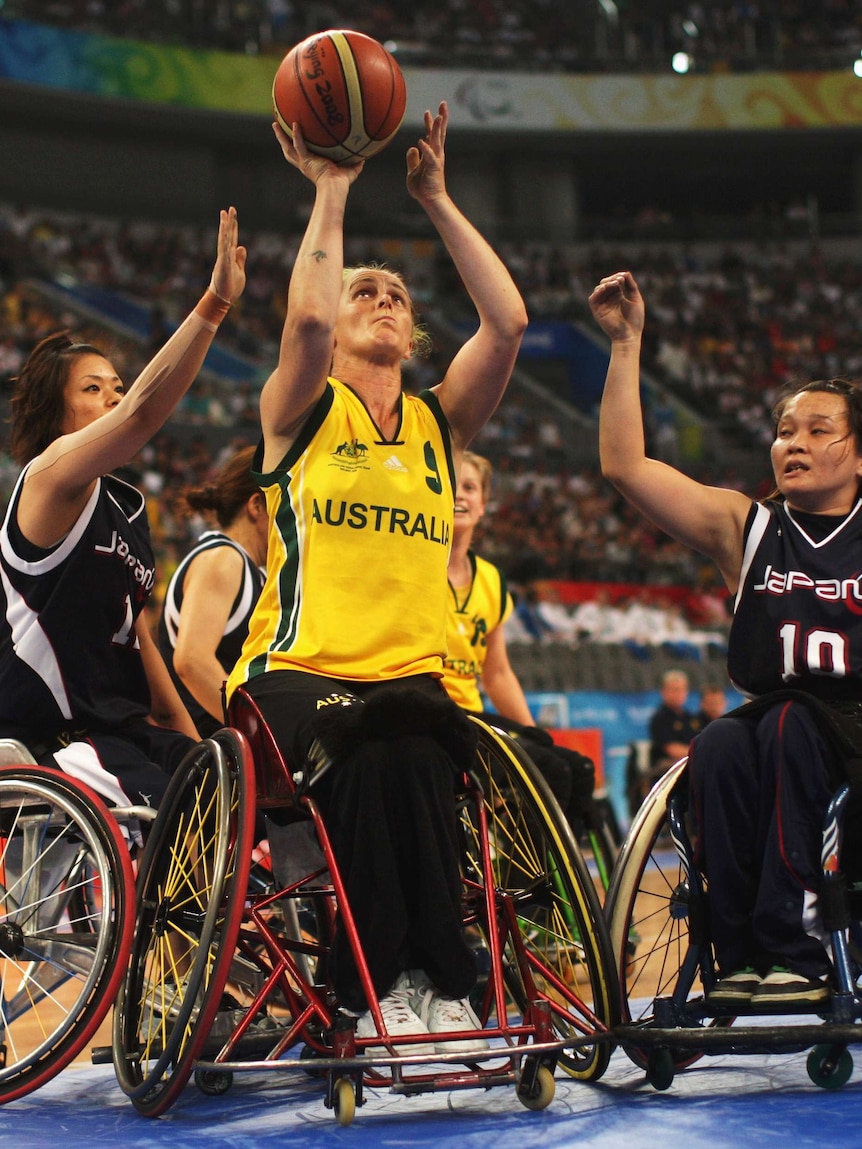 Wheelchair basketball game in stadium. A woman in a top marked 'Australia' shoots while Japanese players attempt to block.