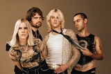 A band of four people poses against a beige backdrop.