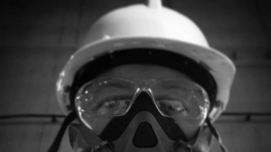A black and white selfie of a man in safety googles, face mask and helmet