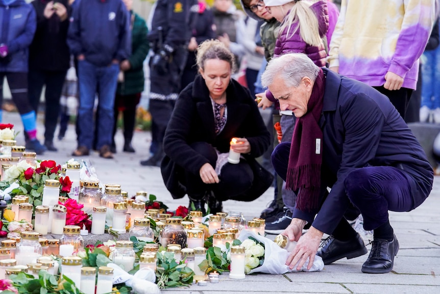 A man adds a wreath and candle to other memorials in a city street.