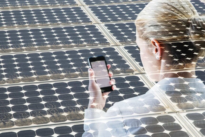 Woman with smart phone in front of a bank of solar cells