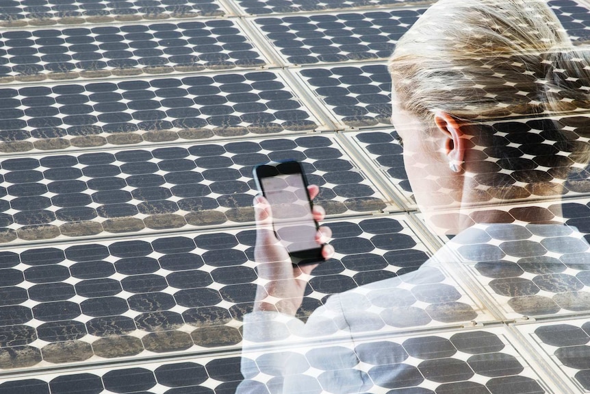 Woman with smart phone in front of a bank of solar cells