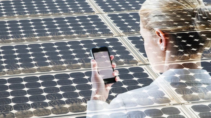 Woman with smart phone in front of a bank of solar cells