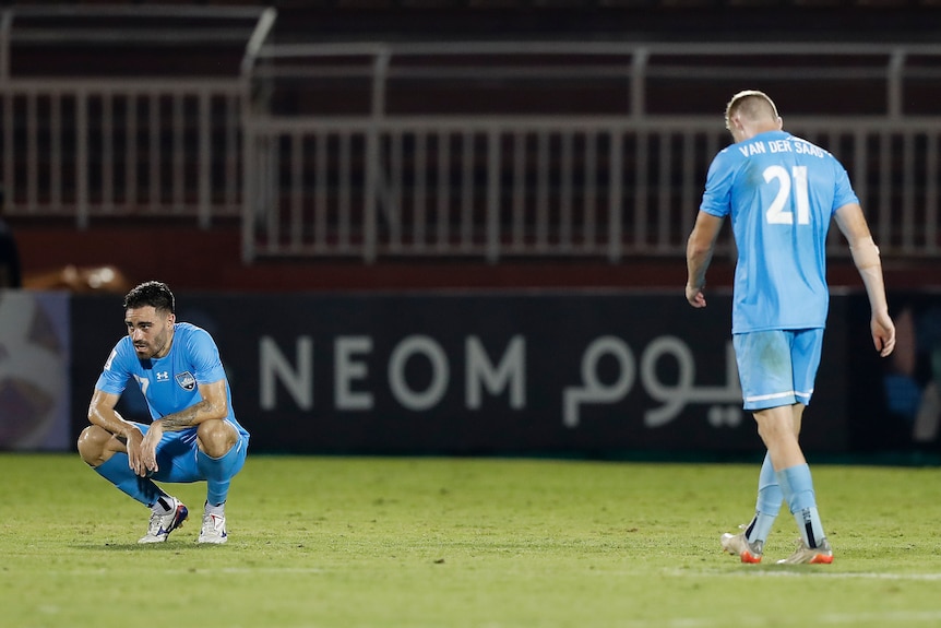 Two soccer players wearing light blue are disappointed after losing a game