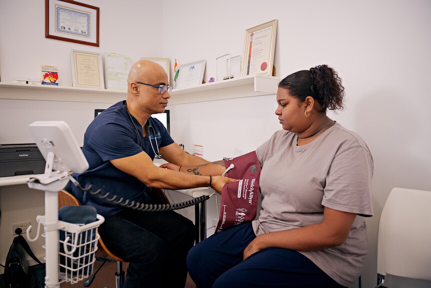 A man in medical scrubs holds a blood pressure band around a woman's arm