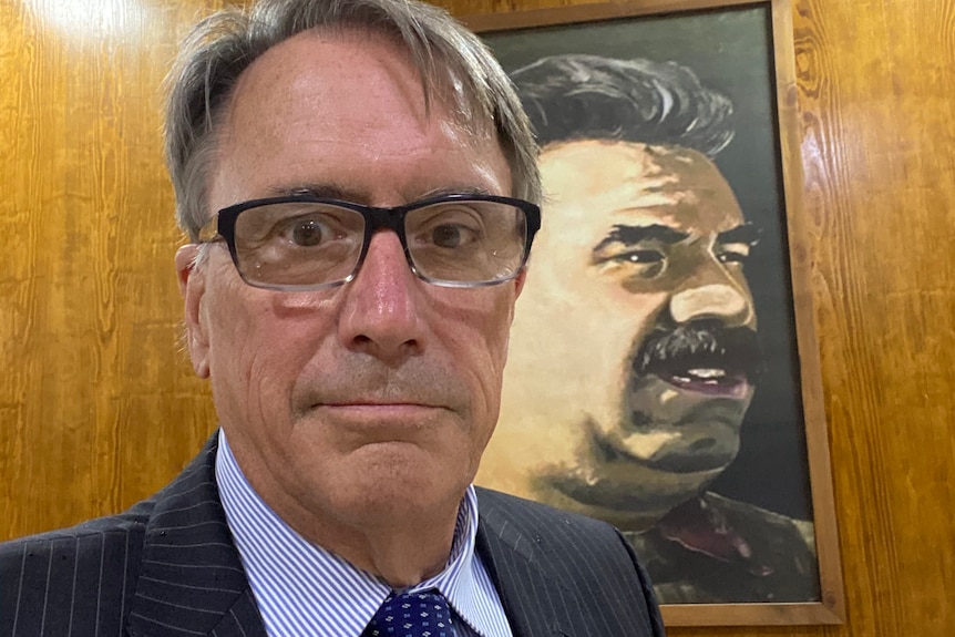 Man in a suit with a painting of a man behind him