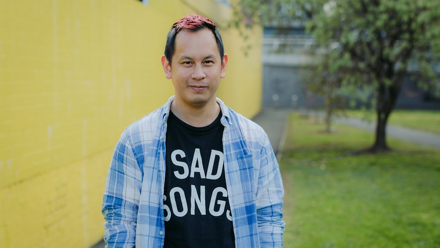 Colour photo of games designer Ken Wong standing outdoors in front in front of yellow wall.