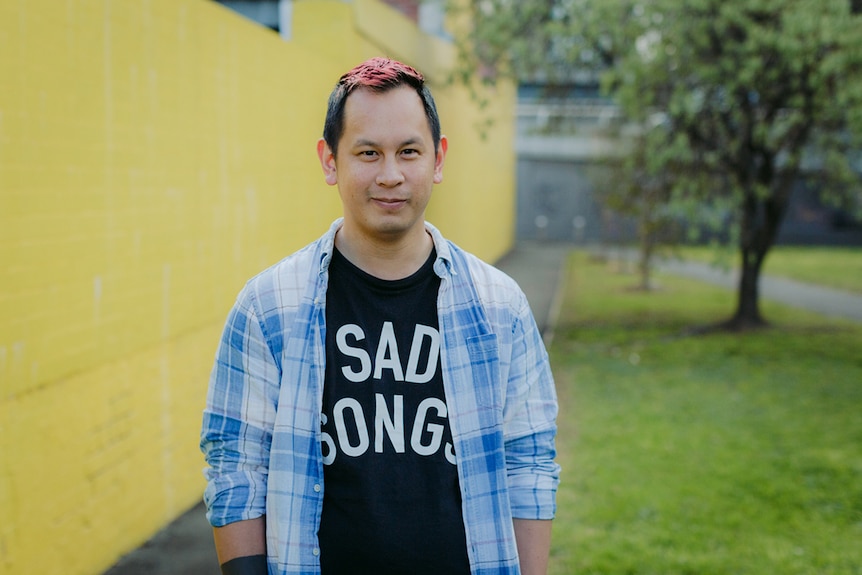 Colour photo of games designer Ken Wong standing outdoors in front in front of yellow wall.