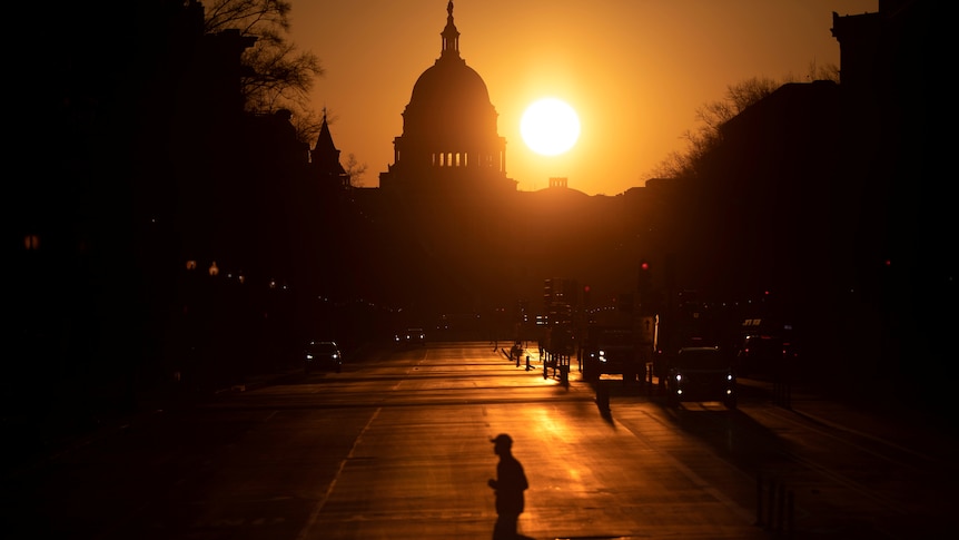 The sun rising over the US Capitol dome, which a runner silhouetted against the sky crossing the street