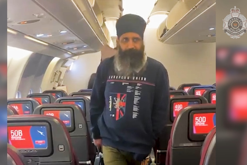 A screenshot of a video of a man walking along the aisle of a plane