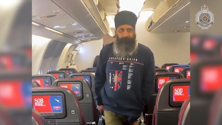 a screenshot of a video of a man walking along the aisle of a plane