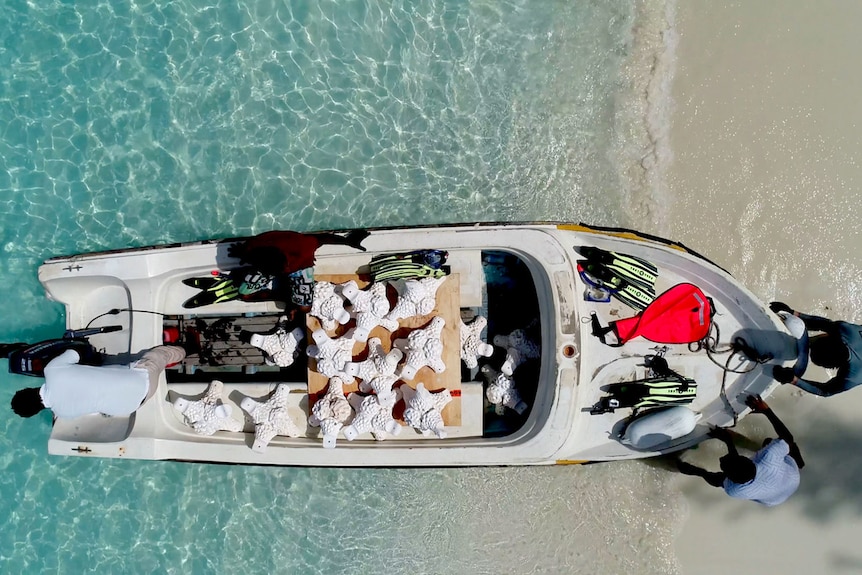 In glittering cyan blue waters, a bird's eye view shows two men pushing a small dinghy loaded with MARS units.