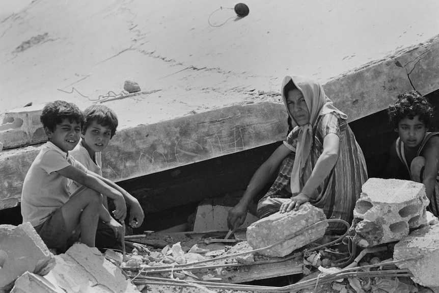 A black and white photo of a Lebanese woman and three children sitting among rubble